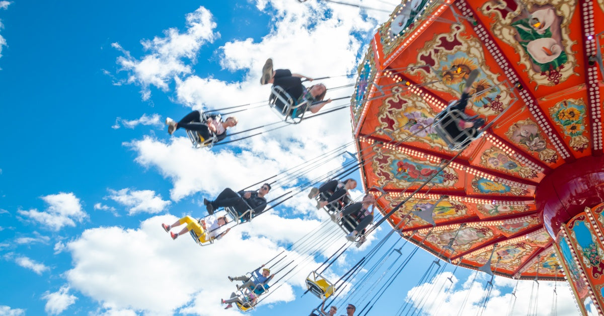 A group of people riding on an amusement park swing attraction. They are in the air, sitting in single and double seats.