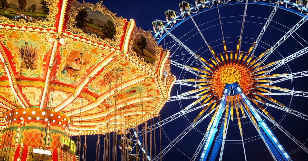 A Ferris wheel and a carousel at a theme park. They are illuminating bright colors against a night sky.