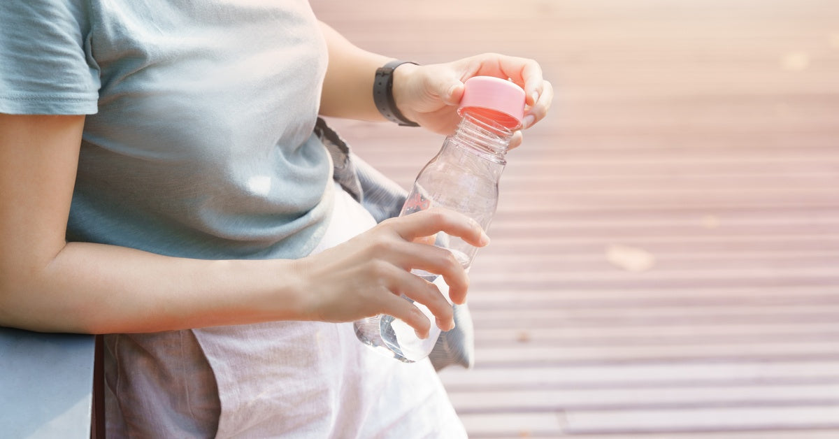 A person opening a plastic water bottle while leaning on a railing outside. The lid of the water bottle is bright pink.