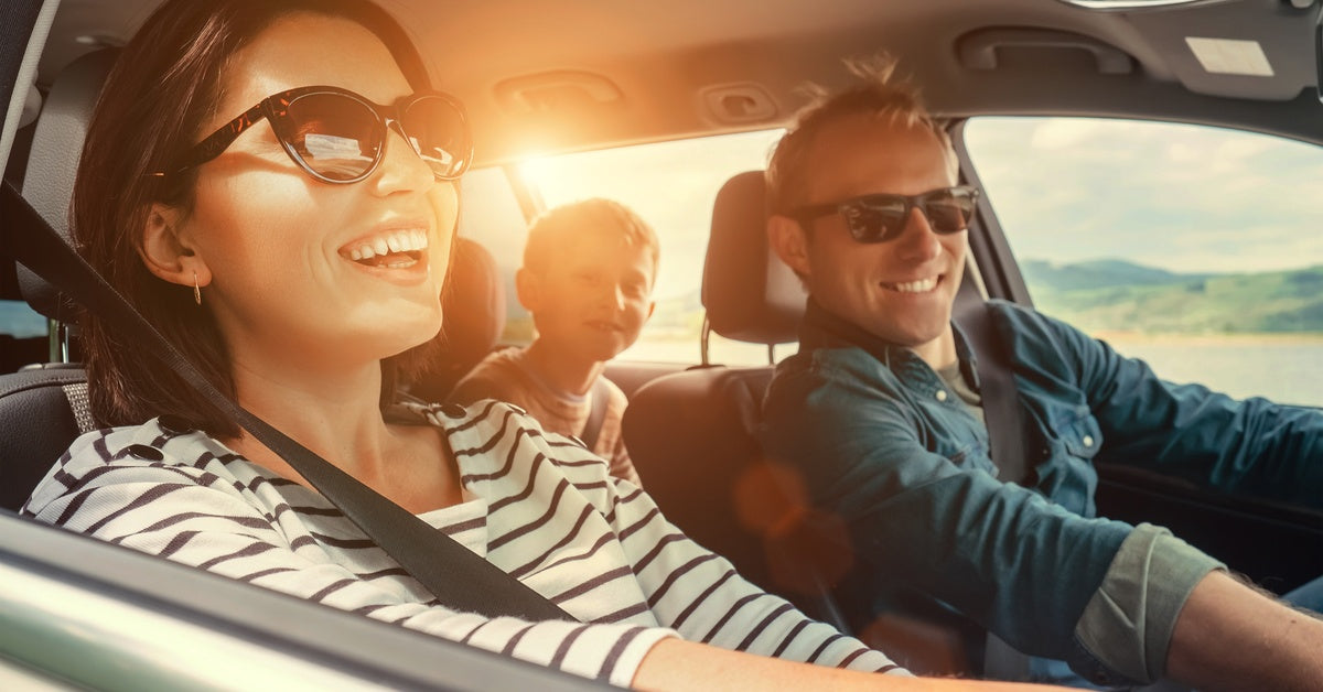 Two adults are sitting in the front seats of a car and wearing sunglasses. A young boy is sitting in the backseat.