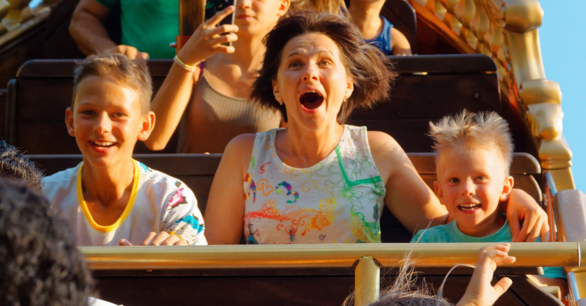 A mom and her two childing riding on a roller coaster. The three of them have excited expressions on their faces.