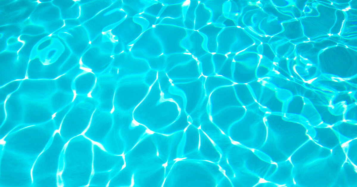 A pool at a water park where nobody is swimming and the sun is shining down, giving the water a vibrant blue appearance.