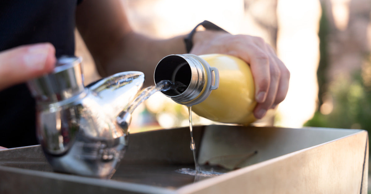 A person filling up their aluminum water bottle at a water fountain. They are shooting water into the bottle from the spout.