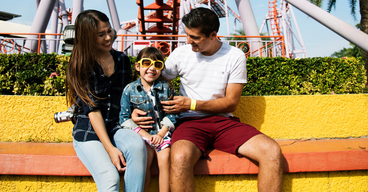 A family sitting in front of a roller coaster at a theme park. They are happily posed for a memorable photo.