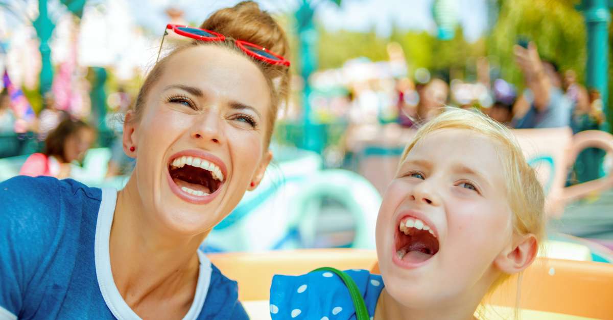 A mother and her daughter at a theme park attraction. They smile and laugh, enjoying the child-friendly ride.