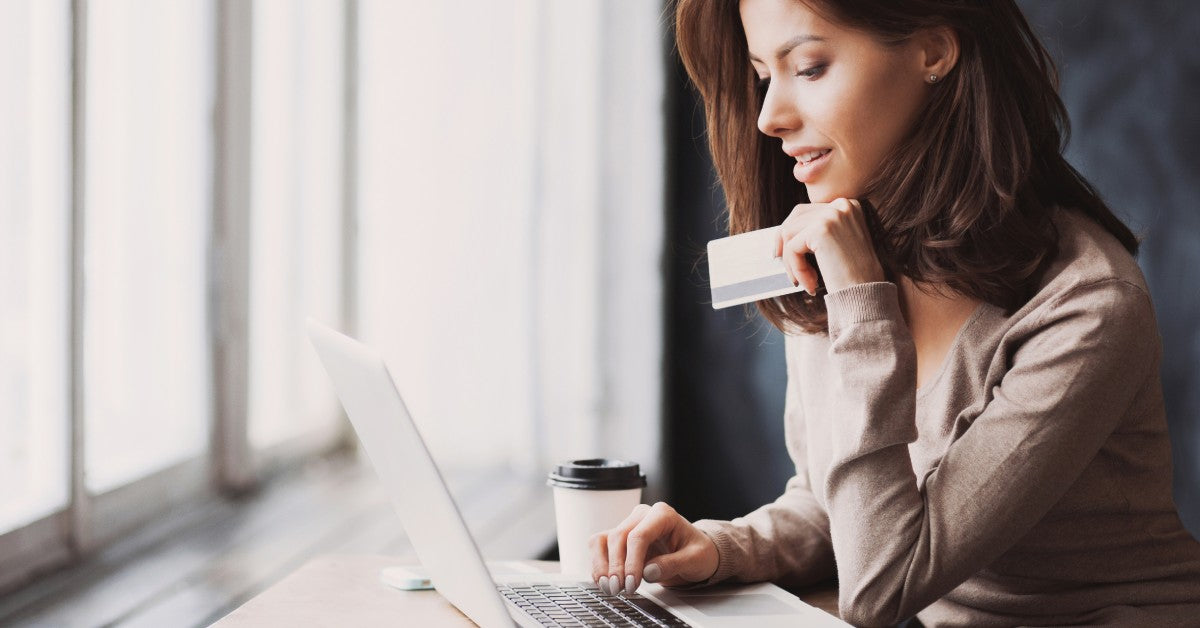 A woman online shopping from her laptop. She is browsing online retailers with her credit card in her hand.