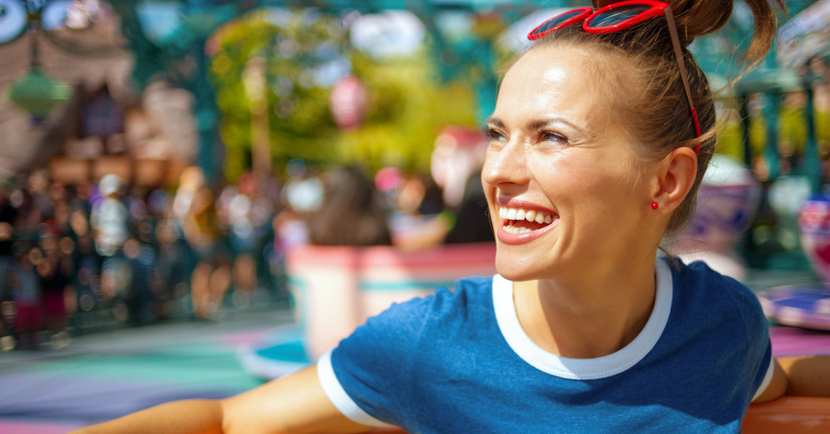 A woman sitting in a teacup ride attraction with other teacups behind her. She is smiling with red sunglasses on her head.