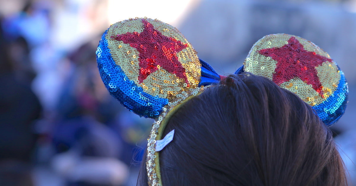 The back of a child's head wearing a headband with mouse ears. The headband has sequins and two red stars in the middle.