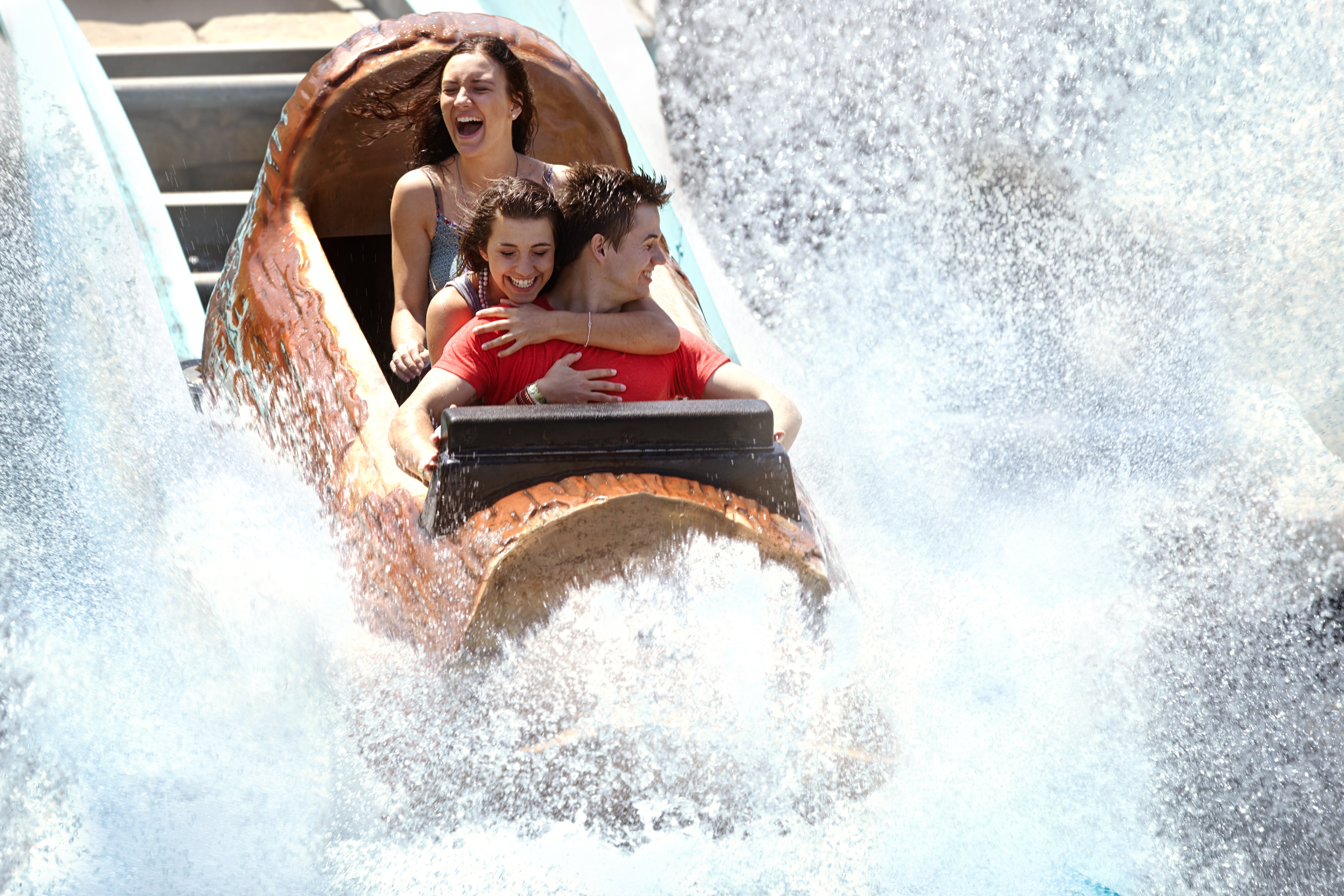 Three people riding on a water ride. They are on a log-shaped cart, plummeting into a pool of water with a big splash.