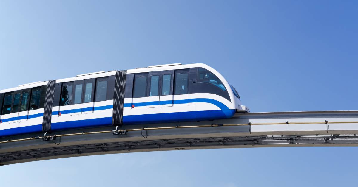 A monorail traveling on a track against a blue sky. The monorail is mostly white with a blue stripe across its body.