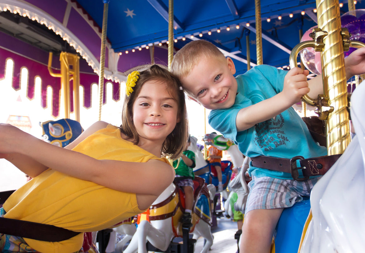 Two children riding on a carousel. They are strapped onto the ride and are holding gold handles at the top of their horses.