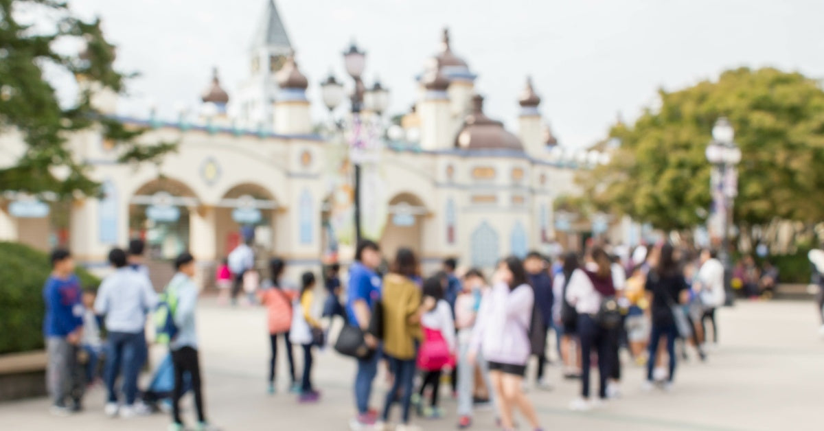 A crowd of people wandering at the front gates to a theme park. The front gates are in the shape of a castle.