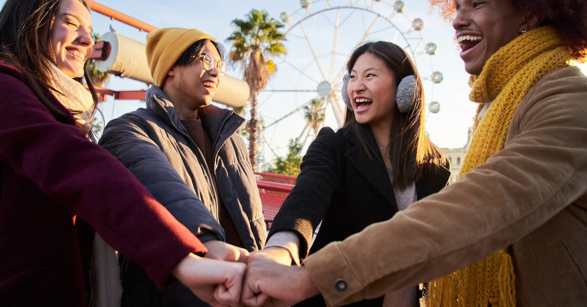 Four adults wearing winter outfits at an amusement park. There is a large Ferris Wheel in the background.