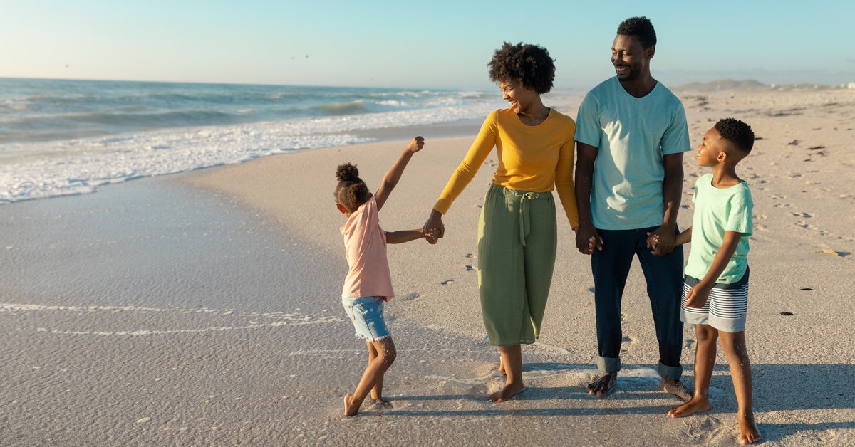 A family walking down a beach, leaving footprints in the sand. They are looking toward the crashing waves.