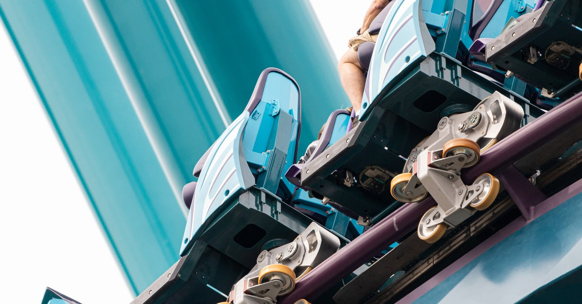 A close-up of a roller coaster with passengers sitting in the seats. The roller coaster has blue seats and purple rails.