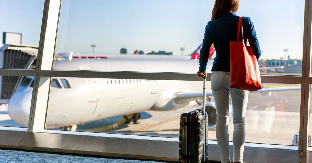 A tourist standing at a large window at an airport and looking at a massive airplane waiting outside.